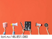 Множество рук с ведром попкорна, кинематографическим хлопком и мегафонами на оранжевом фоне. Стоковое фото, фотограф Pixel_shot / Фотобанк Лори