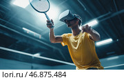 A young man in a yellow sports shirt playing badminton indoors. However, instead of the usual glasses or headband, he is wearing a VR helmet, which creates a futuristic atmosphere. He is focused, his movements are active and dynamic, as if he is completely immersed in a virtual game. The lighting in the gym is bright, with cool blue shades, emphasizing the technological nature of the moment. The composition conveys a combination of traditional sports and modern virtual reality technologies. Стоковое AI-изображение, AI-художник Анна Кривицкая / Фотобанк Лори