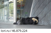 Homeless man in warm clothes sleeping outdoors near the entrance of the building, poverty concept. Стоковое фото, фотограф David Kashakhi / Фотобанк Лори