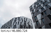Bottom view of modern unique building with triangle shaped windows of black color on bright cloudy sky background. Стоковое фото, фотограф David Kashakhi / Фотобанк Лори