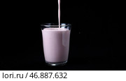 In transparent glass pour viscous pink milkshake on black background. Стоковое фото, фотограф David Kashakhi / Фотобанк Лори