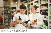 Joyful couple of lovers choose dry or sweet wine in a hypermarket, standing in the department with alcohol against the background of customers. Стоковое видео, видеограф Яков Филимонов / Фотобанк Лори