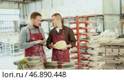 Two enthusiastic young male potters in stained burgundy aprons examining handcrafted ceramic wares in studio and exchanging ideas about techniques of casting. Стоковое видео, видеограф Яков Филимонов / Фотобанк Лори