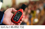 Close up of a man hand holding a red sound level meter and analyzer on clapping audience background. Стоковое фото, фотограф David Kashakhi / Фотобанк Лори