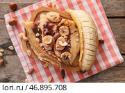 Доска вкусных тонких блинчиков с шоколадной пастой, нарезанным бананом и орехами на деревянном фоне. Стоковое фото, фотограф Pixel_shot / Фотобанк Лори