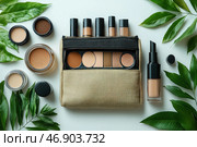 A set of cosmetics in natural beige and brown shades, located on a light background. In the center is a cosmetic bag made of natural fabric with a black zipper, partially open, showing a palette of eyeshadows and several tubes of foundation or concealer. Around the cosmetic bag are neatly laid out jars of creams, compact eyeshadows, and a bottle of liquid foundation. There are also green leaves in the frame, creating an atmosphere of naturalness and eco-friendliness. Стоковое AI-изображение, AI-художник Анна Кривицкая / Фотобанк Лори