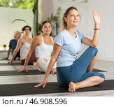Calm European middle-aged woman practicing Half Lord of the fishes pose or Ardha Matsyendrasana during group yoga training. Стоковое фото, фотограф Яков Филимонов / Фотобанк Лори