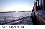 A boat with a small amount of snow on it floating forward on which the waves of the river break apart and from afar you can see the outgoing bright sun and the forest. Стоковое фото, фотограф David Kashakhi / Фотобанк Лори