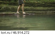 Side view of a man walking barefoot on wet rocks near mountainous water stream. Стоковое фото, фотограф David Kashakhi / Фотобанк Лори