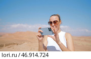 Tourist woman using cell phone for shooting, standing in desert. Стоковое фото, фотограф David Kashakhi / Фотобанк Лори