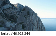 Gorgeous view of the mountain slopes covered with small trees and green moss and large cliff near the sea against blue sky. Стоковое фото, фотограф David Kashakhi / Фотобанк Лори