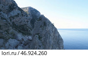 Gorgeous view of the mountain slopes covered with small trees and green moss and large cliff near the sea against blue sky. Стоковое фото, фотограф David Kashakhi / Фотобанк Лори