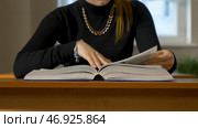 Woman sitting at the table leafing through the book. Стоковое фото, фотограф David Kashakhi / Фотобанк Лори