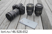 Moscow - Russia, 10.10.2021: new Nikon camera with lens and a modern Iphone 13 pro max lying outdoors on a wooden surface. Редакционное фото, фотограф David Kashakhi / Фотобанк Лори