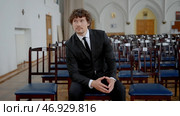 Young man with curly hair in black and white classic suit in empty church. Стоковое фото, фотограф David Kashakhi / Фотобанк Лори
