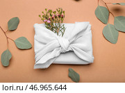 Подарочная коробка, обернутая тканью, цветами и ветками эвкалипта на цветном фоне. Стоковое фото, фотограф Pixel_shot / Фотобанк Лори