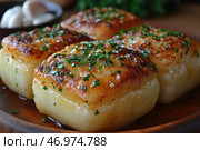 Crispy, browned cubes of potato, topped with freshly chopped herbs and coarse sea salt. The surface of the potato is slick with oil, highlighting its delicious appearance. Garlic and fresh herbs can be seen around the wooden plate, hinting at the aromatic seasoning. The dish looks rich, with a crispy crust on the outside and a soft texture on the inside. The background is slightly blurred, creating a focus on the delicious appetizer. Стоковое AI-изображение, AI-художник Анна Кривицкая / Фотобанк Лори