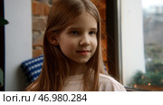 Beautiful smiling girl touching her long hair and posing by the window. Стоковое фото, фотограф David Kashakhi / Фотобанк Лори
