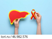 Женщина с лентой осведомленности и бумажной печенью на синем фоне. Концепция гепатита. Стоковое фото, фотограф Pixel_shot / Фотобанк Лори