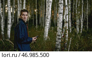 Young man walks in woods with phone and looks around anxiously. Стоковое фото, фотограф David Kashakhi / Фотобанк Лори
