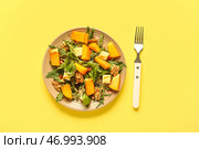 Тарелка вкусного салата с хурмой, гранатовыми зернами и грецким орехом на желтом фоне. Стоковое фото, фотограф Pixel_shot / Фотобанк Лори