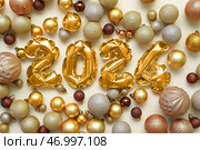 Композиция с фигурой 2024 сделана из фольгированных шаров и рождественских шаров на бежевом фоне. Стоковое фото, фотограф Pixel_shot / Фотобанк Лори