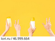 Женские руки с бутылками солнцезащитного крема, показывающие жест победы на желтом фоне. Стоковое фото, фотограф Pixel_shot / Фотобанк Лори