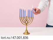 Мужчина зажигает свечи в меноре на розовом фоне, крупным планом. Празднование Хануки. Стоковое фото, фотограф Pixel_shot / Фотобанк Лори