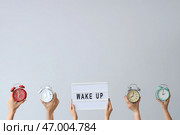 Руки, держащие различные будильники, и доска с надписью ВСТАВАЙ на сером фоне. Стоковое фото, фотограф Pixel_shot / Фотобанк Лори