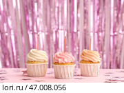 Сладкие праздничные капкейки с горящими свечами и мишурой на розовом фоне. Стоковое фото, фотограф Pixel_shot / Фотобанк Лори