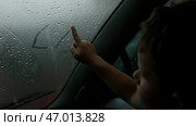 The child draws pictures with his finger on a wet misted window on a cloudy day. Стоковое фото, фотограф David Kashakhi / Фотобанк Лори