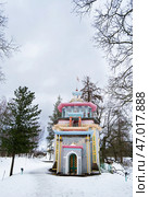 A vibrant, multi-colored The Squeaky Gazebo is set against a backdrop of snow-covered ground and leafless trees in Tsarskoe Selo. Редакционное фото, фотограф Зворыгина Елена / Фотобанк Лори