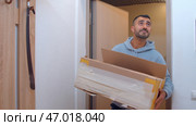 An adult handsome man in oversize clothes brought boxes to a new apartment. Стоковое фото, фотограф David Kashakhi / Фотобанк Лори