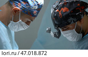 Close up shot of doctor in surgical loupe, sterile mask and protective hair cover looking at the camera. Стоковое фото, фотограф David Kashakhi / Фотобанк Лори