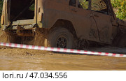 The off-road vehicle drives through a muddy obstacle course. The vehicle is kicking up clouds of mud as it traverses the difficult terrain. Red and white striped tape marks the boundary of the strip. Стоковое фото, фотограф Воловодов Владимир / Фотобанк Лори