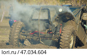 A muddy off-road vehicle stuck in a ditch with smoke billowing from its engine. The vehicle is covered in mud and appears to be overheating. Extreme off-roading competition. Стоковое фото, фотограф Воловодов Владимир / Фотобанк Лори