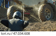 A person in a helmet pulls a rope attached to a muddy off-road vehicle stuck in a ditch. The vehicle is covered in mud and dust, and the person is struggling to pull it out. Стоковое фото, фотограф Воловодов Владимир / Фотобанк Лори