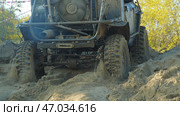 A muddy off-road vehicle navigates a challenging sandy terrain. The vehicle's tires are deeply embedded in the sand, and the suspension is flexed as it climbs the slope. Стоковое фото, фотограф Воловодов Владимир / Фотобанк Лори