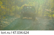 A muddy SUV drives through the sand with dense woods kicking up dust. Sunlight streams through the trees, casting spectacular shadows. Rear view. Extreme off-road racing. Стоковое фото, фотограф Воловодов Владимир / Фотобанк Лори