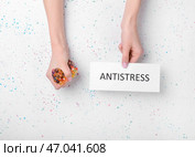 Женские руки сжимают стресс-мяч и лист бумаги со словом АНТИСТРЕССА на светлом фоне. Стоковое фото, фотограф Pixel_shot / Фотобанк Лори