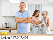 An adult daughter, together with an elderly mother, scolds an elderly father while he is preparing dinner in kitchen. Стоковое фото, фотограф Яков Филимонов / Фотобанк Лори