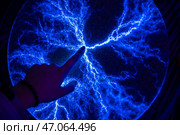 Hand touching a plasma display, creating mesmerizing blue electrical discharges in a dark environment, showcasing the fascinating interaction between electricity and human touch. Стоковое фото, фотограф Ольга Ильина / Фотобанк Лори