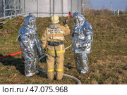 Пожарные в защитных костюмах занимают позиции для тушения пожара. Пожарные в теплоотражающих костюмах на фоне нефтяного резервуара на нефтехимическом заводе. Отделение пожарных. Стоковое фото, фотограф Эдуард Белкин / Фотобанк Лори