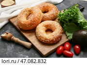 Деревянная доска с вкусными бубликами с кунжутом и свежими овощами на черном фоне. Стоковое фото, фотограф Pixel_shot / Фотобанк Лори