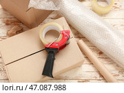 Диспенсер упаковочной ленты, картонные коробки и рулон пузырчатой пленки на деревянном фоне. Стоковое фото, фотограф Pixel_shot / Фотобанк Лори