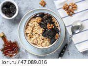 Чаша вкусной овсянки с черносливом, грецкими орехами и бутылкой кленового сиропа на сером фоне. Стоковое фото, фотограф Pixel_shot / Фотобанк Лори