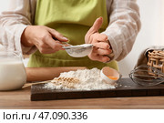 Женщина просеивает муку для приготовления теста на кухонном столе. Стоковое фото, фотограф Pixel_shot / Фотобанк Лори