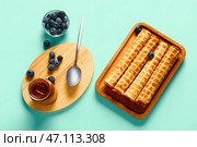 Доска с вкусными вафельными трубочками, черникой и банкой вареной сгущенки на бирюзовом фоне. Стоковое фото, фотограф Pixel_shot / Фотобанк Лори