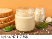 Банки с вкусной тахини, семенами кунжута, хлебом и шпинатом на деревянном столе возле цветной стены, крупным планом. Стоковое фото, фотограф Pixel_shot / Фотобанк Лори