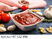 Чаша вкусной томатной пасты, зубчики чеснока и сырые макароны фарфалле на сером фоне гранж. Стоковое фото, фотограф Pixel_shot / Фотобанк Лори